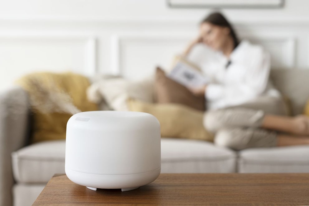 White aroma diffuser on table with woman reading on sofa behind