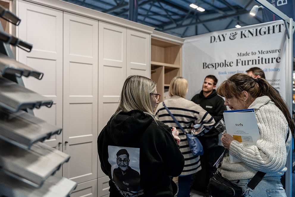 Visitors browsing beside the cabinet-handle sample display at the stand, with cream panelled fitted wardrobes behind