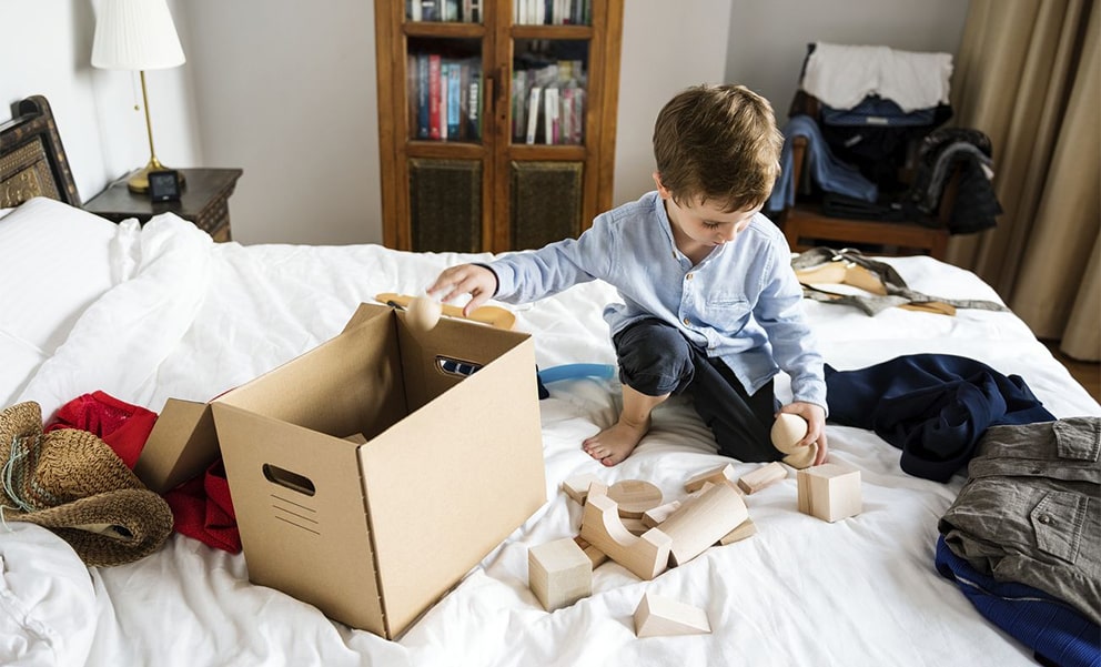 Young boy packing wooden blocks into a cardboard box on a bed