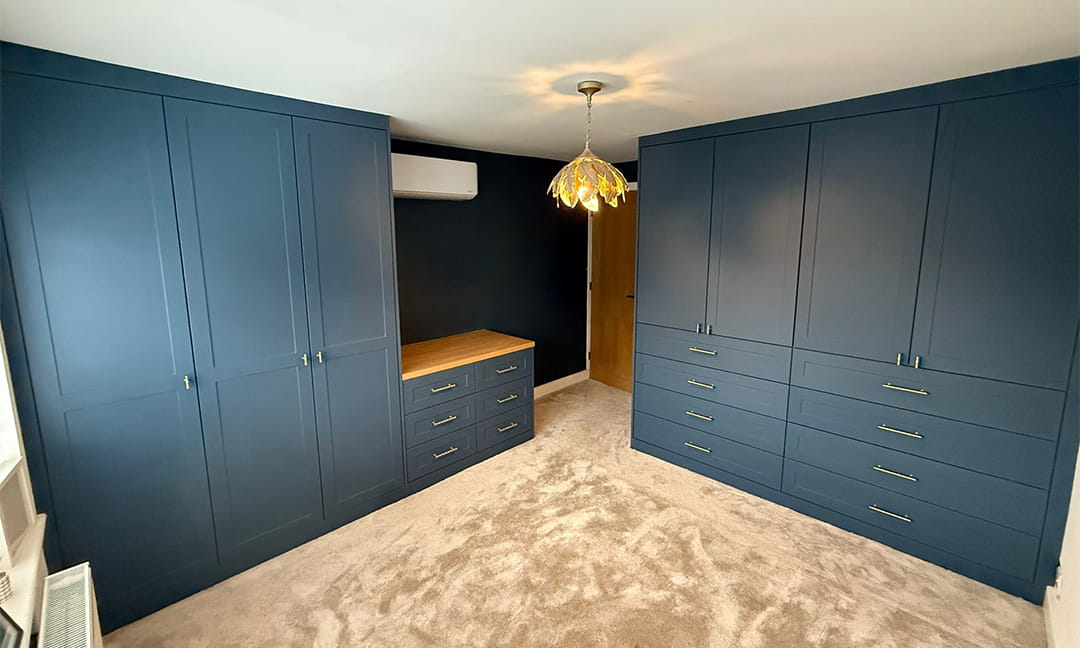 Two blue fitted wardrobe runs with oak-topped drawer chest between