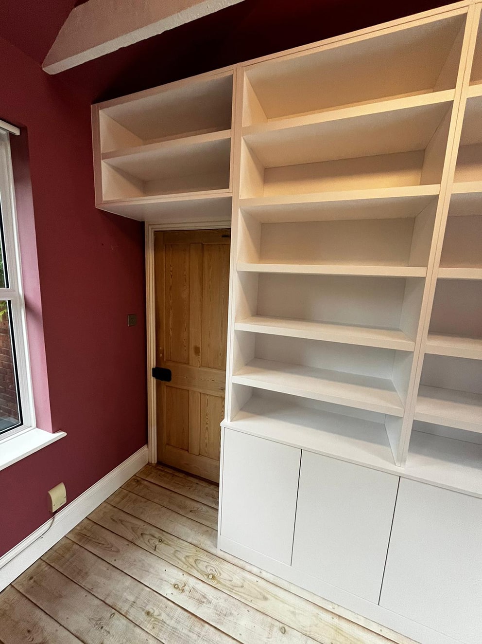 White bookshelving spanning over doorway in burgundy room