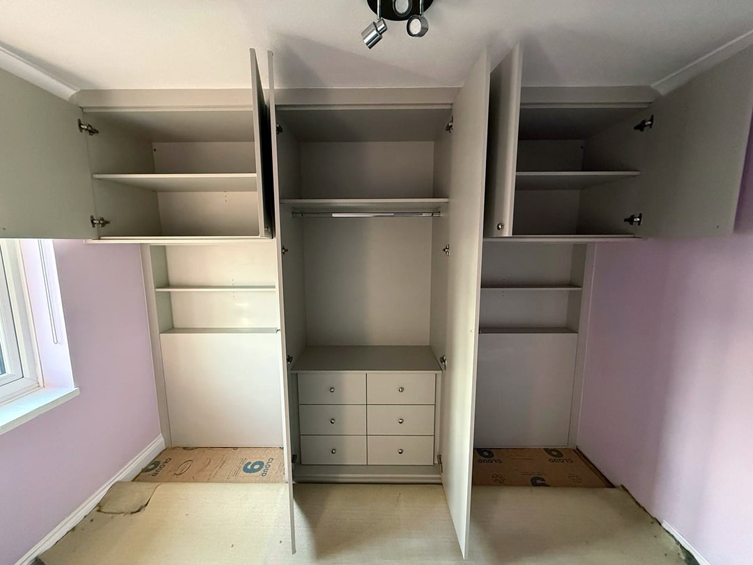Open grey overbed wardrobes showing shelves and drawers