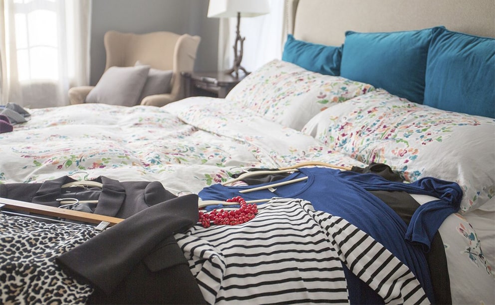 Clothes and hangers piled on a floral unmade bed