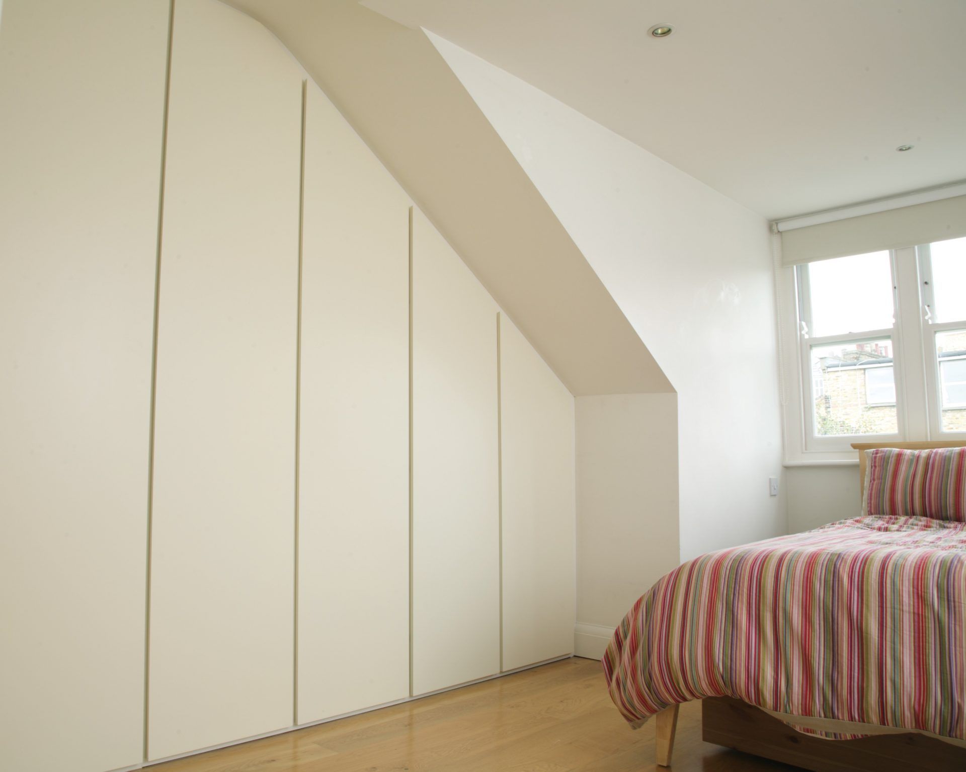 White handleless wardrobes following sloped loft ceiling
