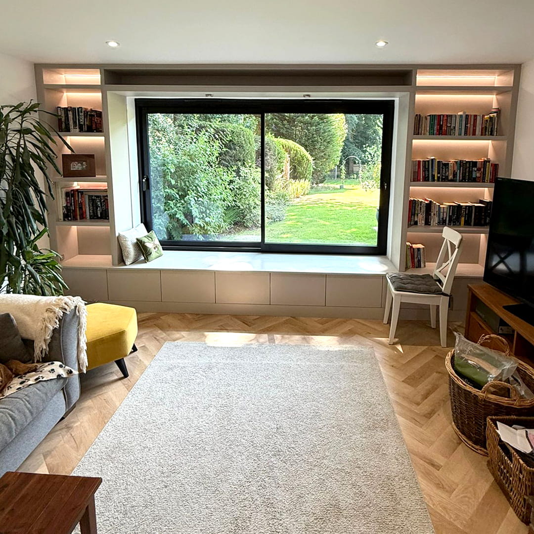 Living room window seat with storage drawers flanked by lit bookshelves